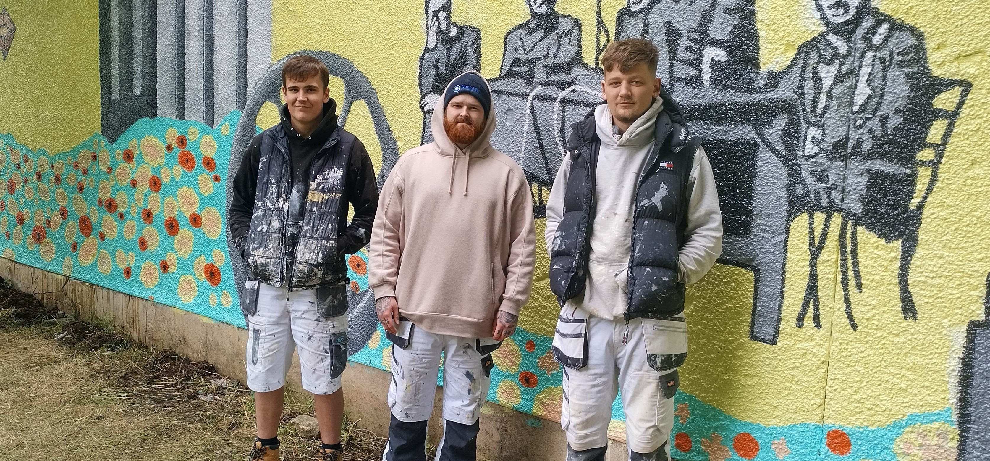 Three students pose outside the mural.