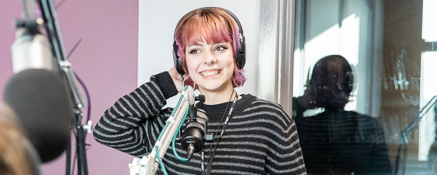 Image shows young student presenting in a studio, smiling.